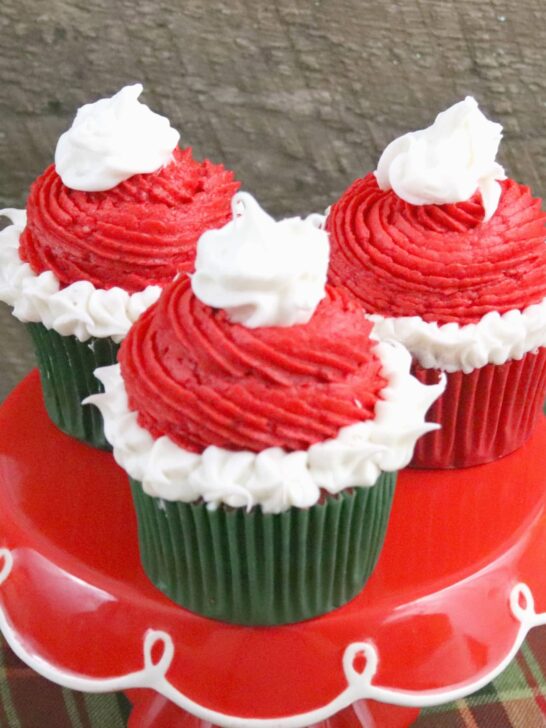 These fun a festive Santa hat Christmas Cupcakes are super fun to make with kids! The recipe features a cocoa buttercream frosting perfect for the season! The red and green inside makes a fun treat for kids! #holidaybaking #christmascupcakes #