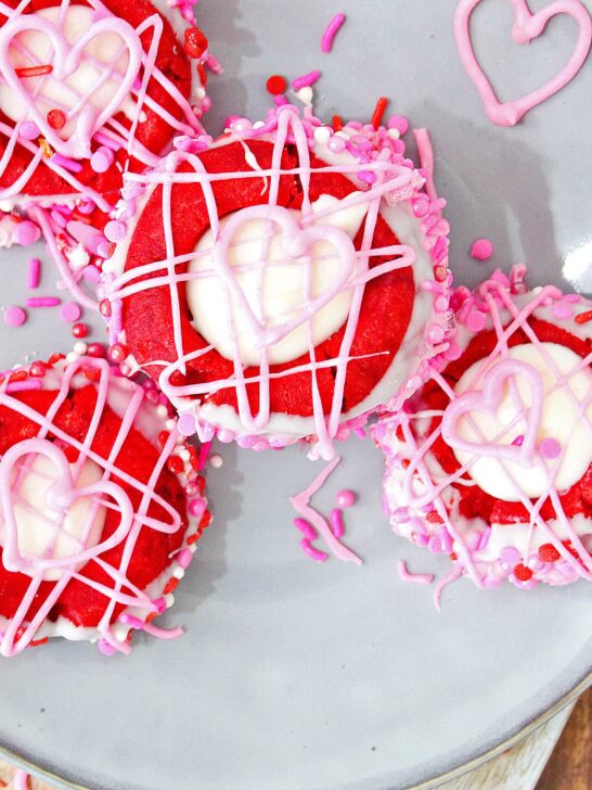 These fun and delicious thumbprint Valentine's Day cookies are a bright red color and decorated with white, red and pink sprinkles. They are perfect to take for a school snack for your kids (Valentine's Day is on a Friday this year!). Or even a for a classroom party. You can make these for the household or even a special treat for your coworkers. #valentinesday #vday #valentinecookies
