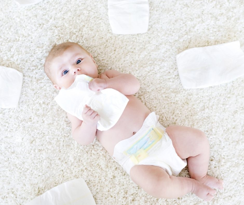 baby laying down looking up with diaper in mouth