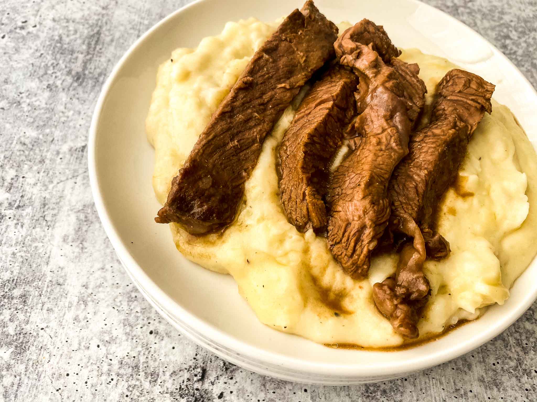 Crockpot Sirloin Steak on mashed potatoes on a white round plate