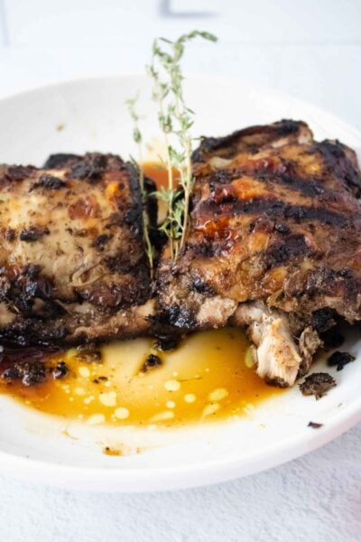 two pieces of jerk chicken on a white round plate with two sprigs of thyme for garnish